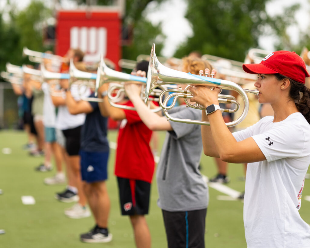 A medium skin tone woman plays a brass instrument with others outside.