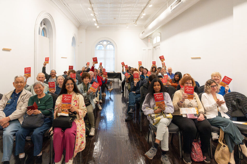 A group of about 40 seated people hold up books to the camera