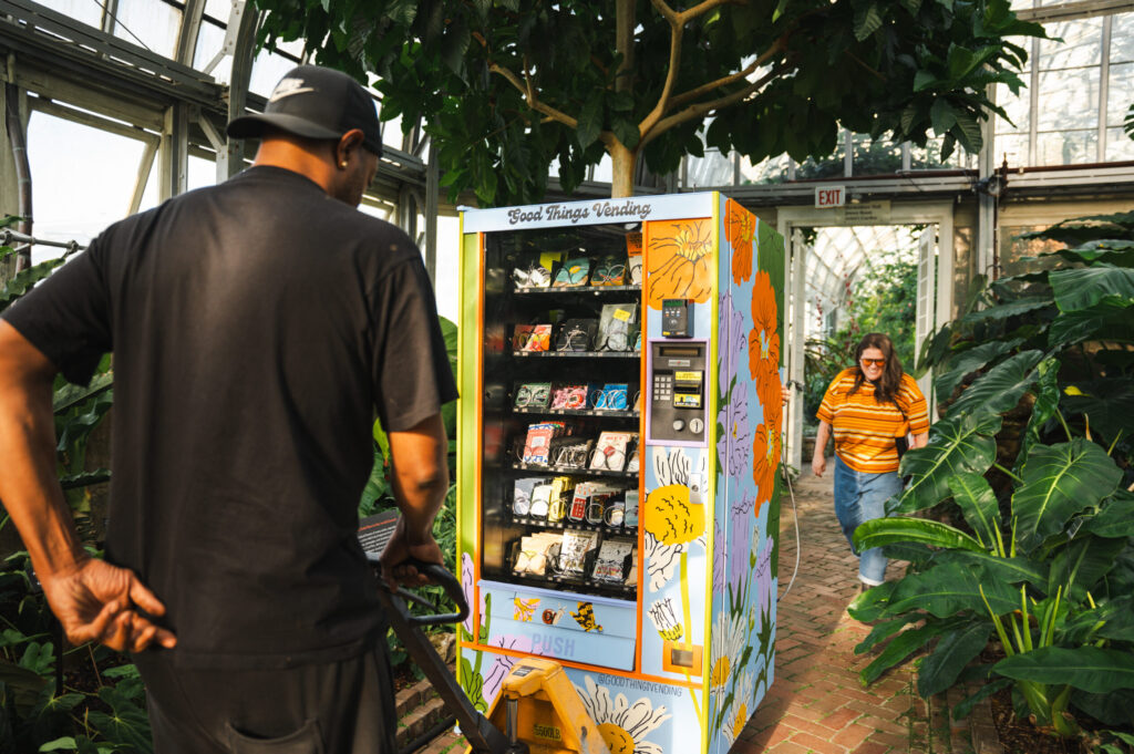 Two people hauling a vending machine into an arboretum.