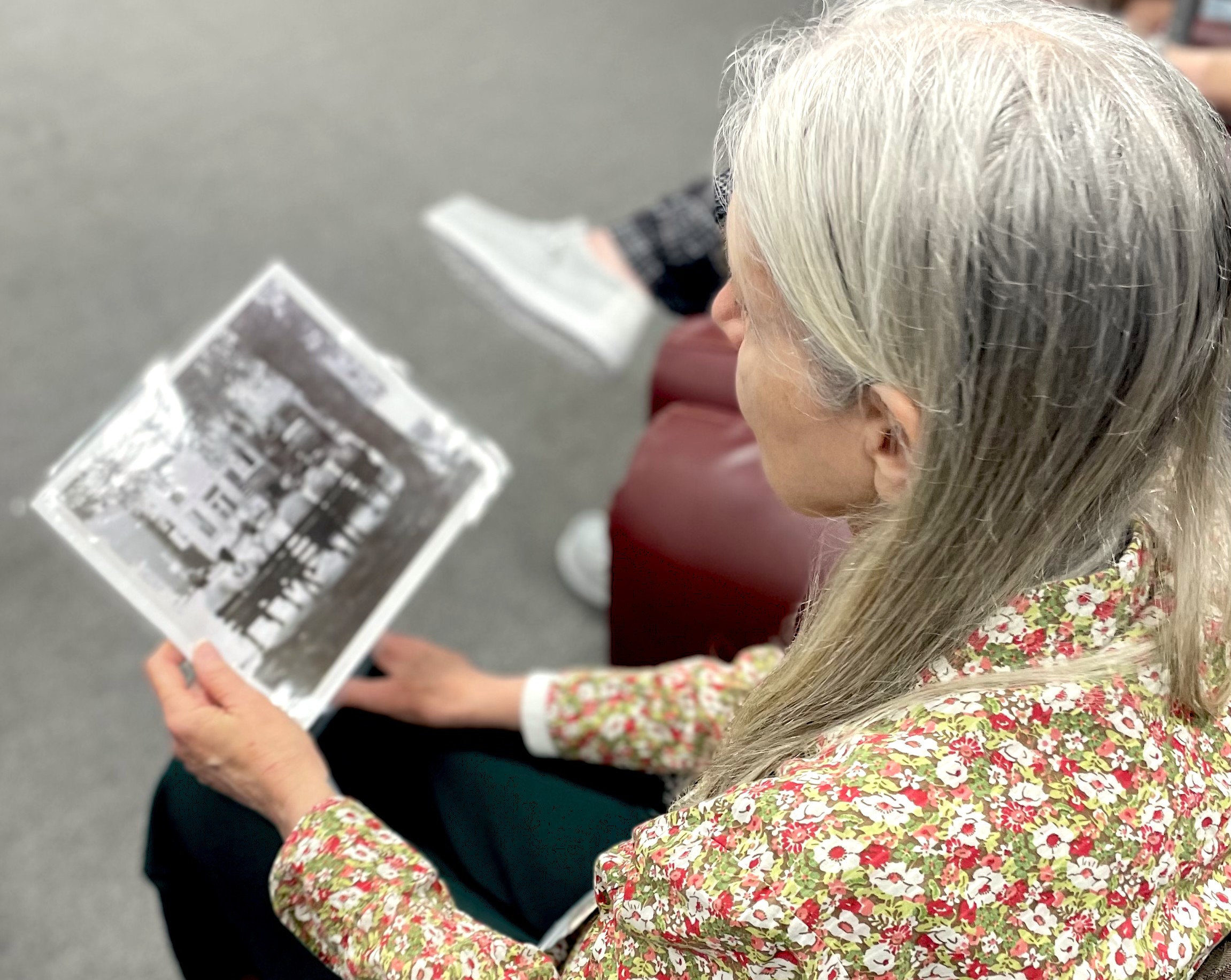 A woman with silver hair holding a black and white photograph.