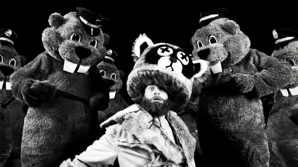 A man in a large raccoon-style hat is surrounded by beaver mascots wearing police caps.