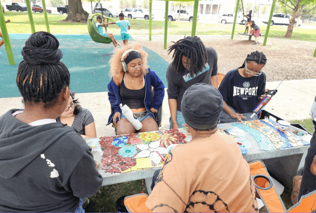 Several people creating art around a table outside.