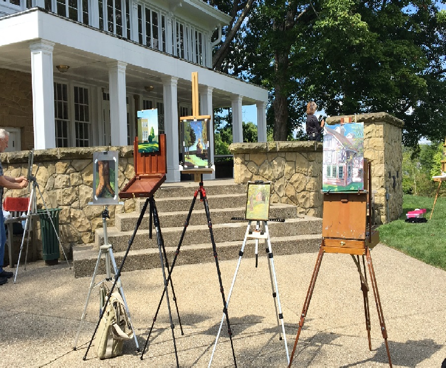 Canvases and easels set up outside a mansion.
