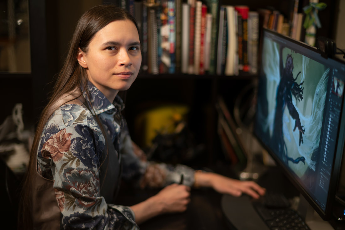 A woman with medium skin tone witting at a desk with a desktop monitor.