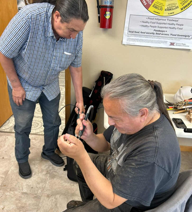 A person standing next to another who is sitting and working with their hands.