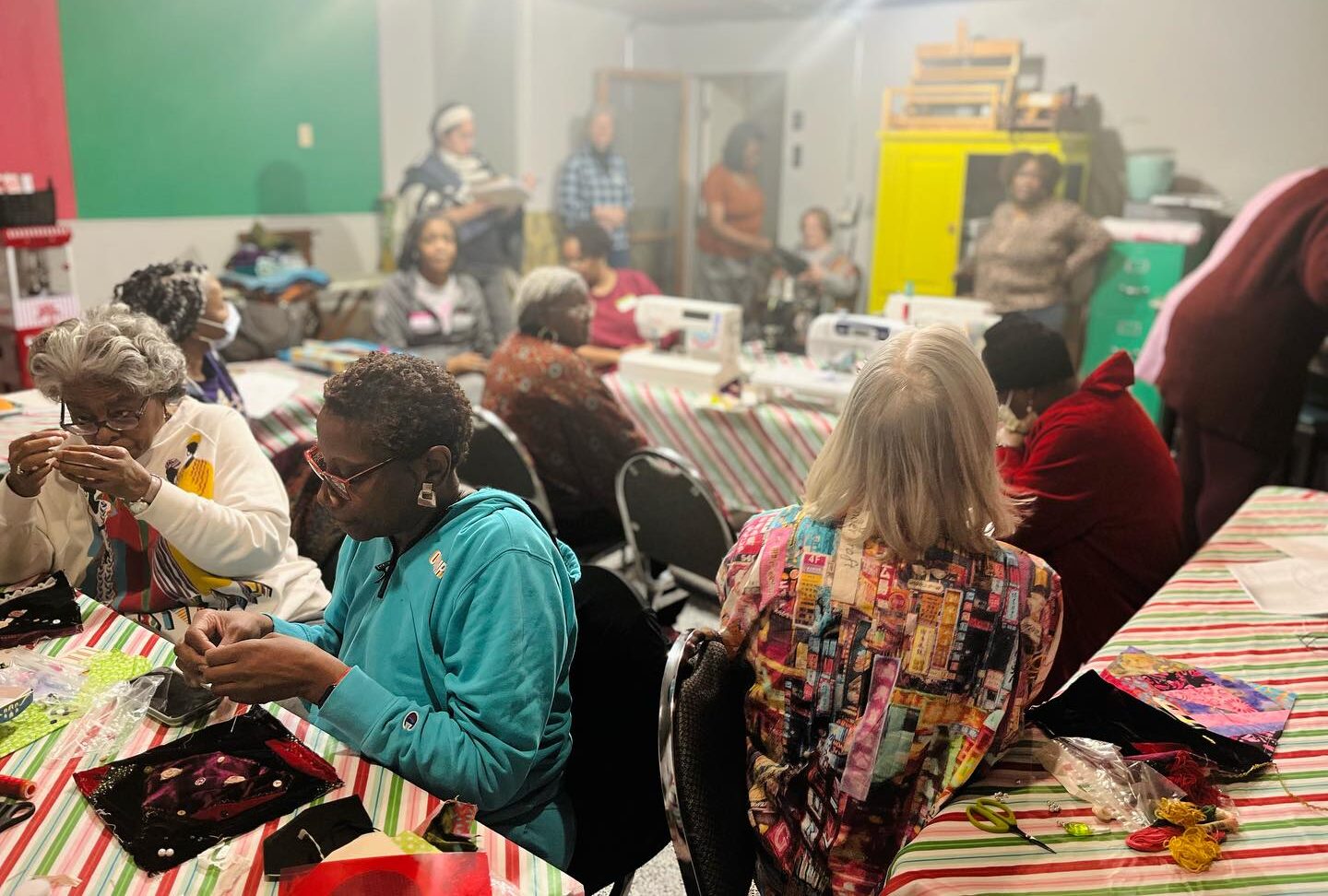 Women sitting indoors and quilting at tables.