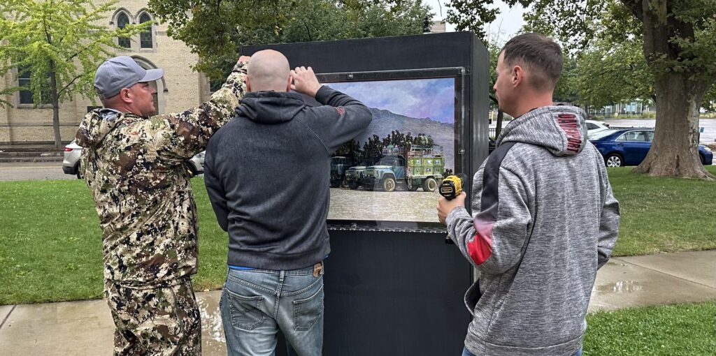 Three veterans mounting an original painting at an outdoor installation.