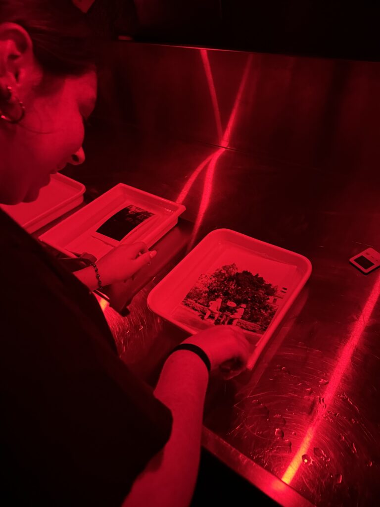 A person smiling in a darkroom with red light on a table.