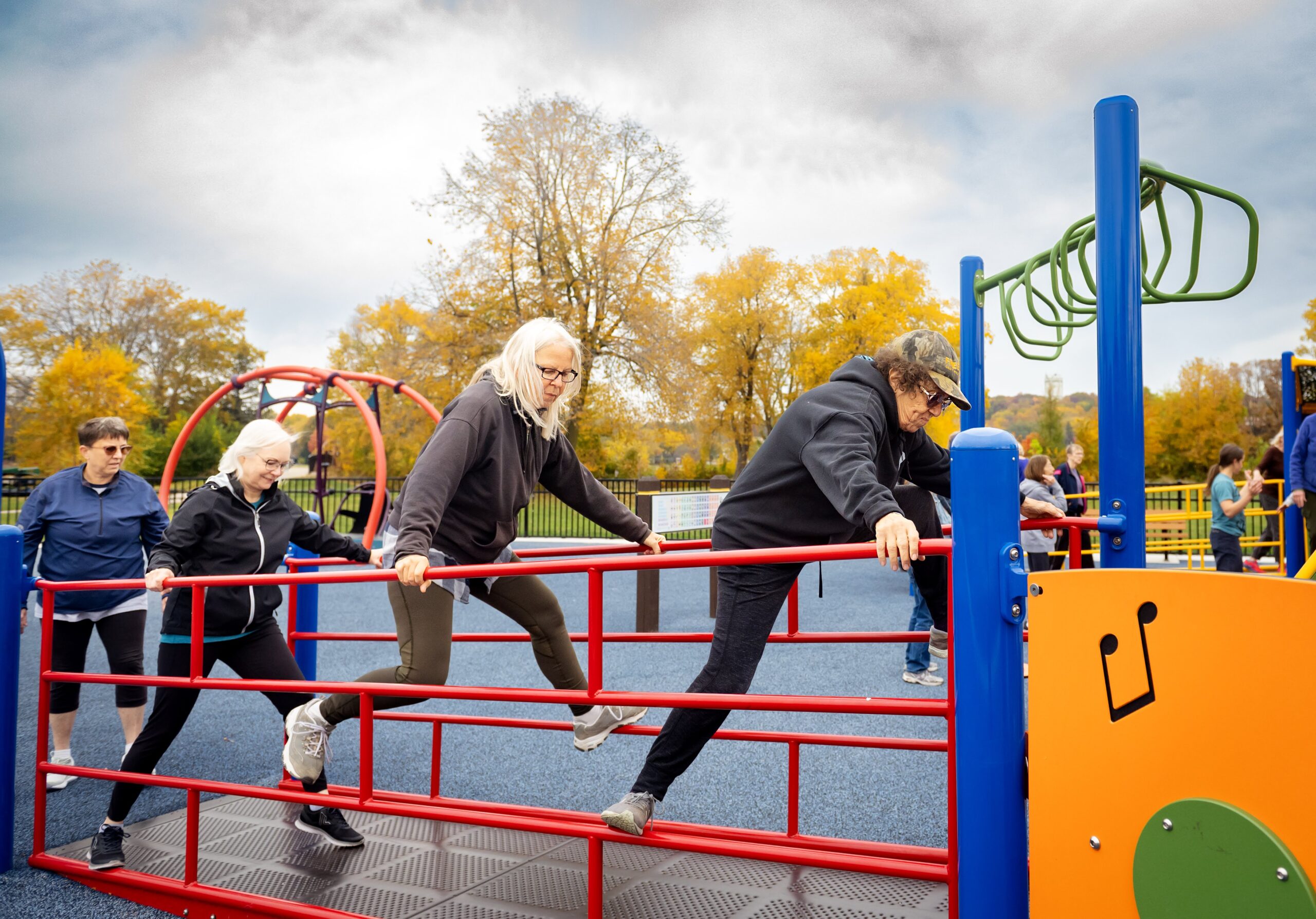 Three older people climbing on railings at a playground