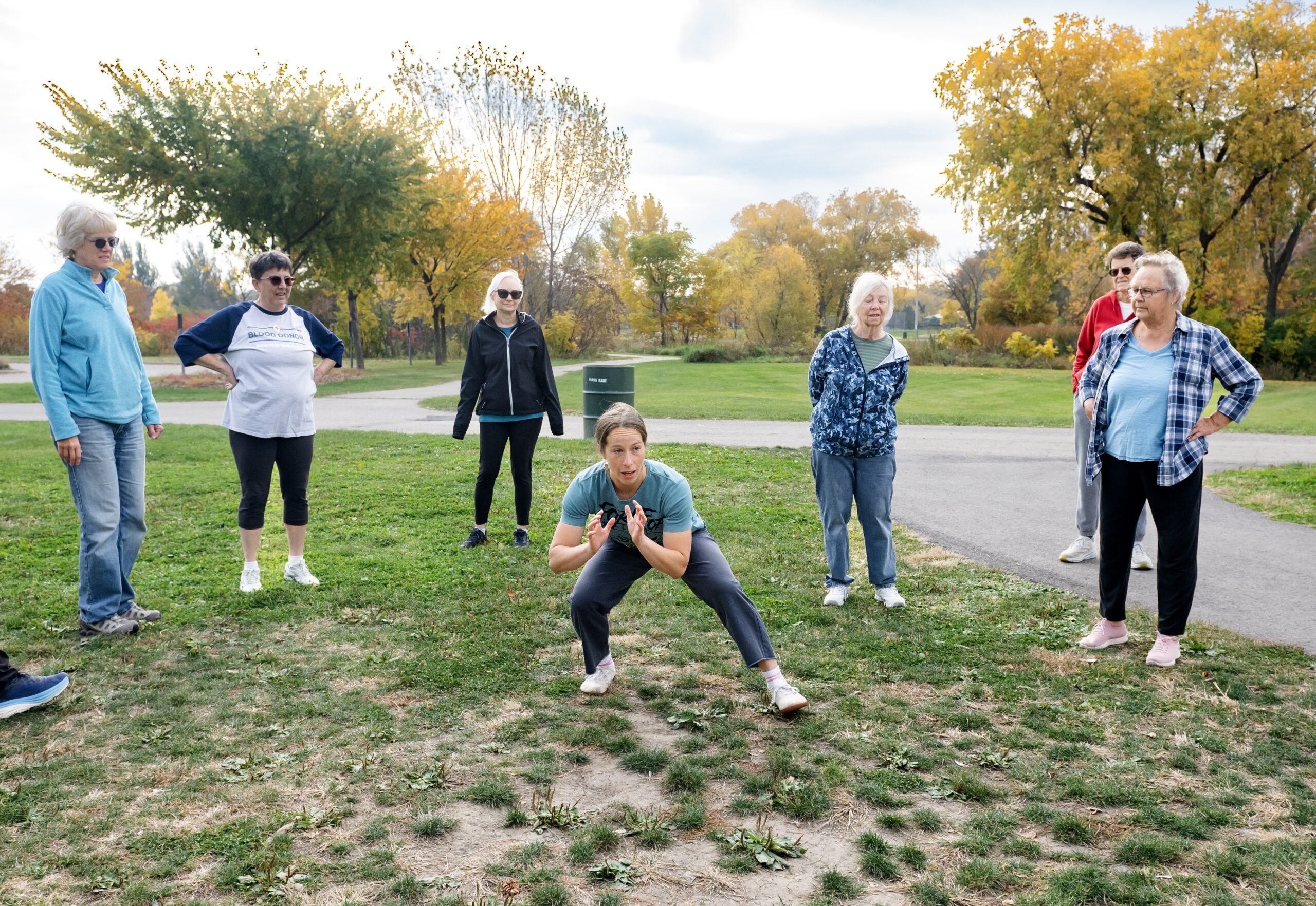 A group of seniors outdoors watching a person at the center showing them a movement exercise