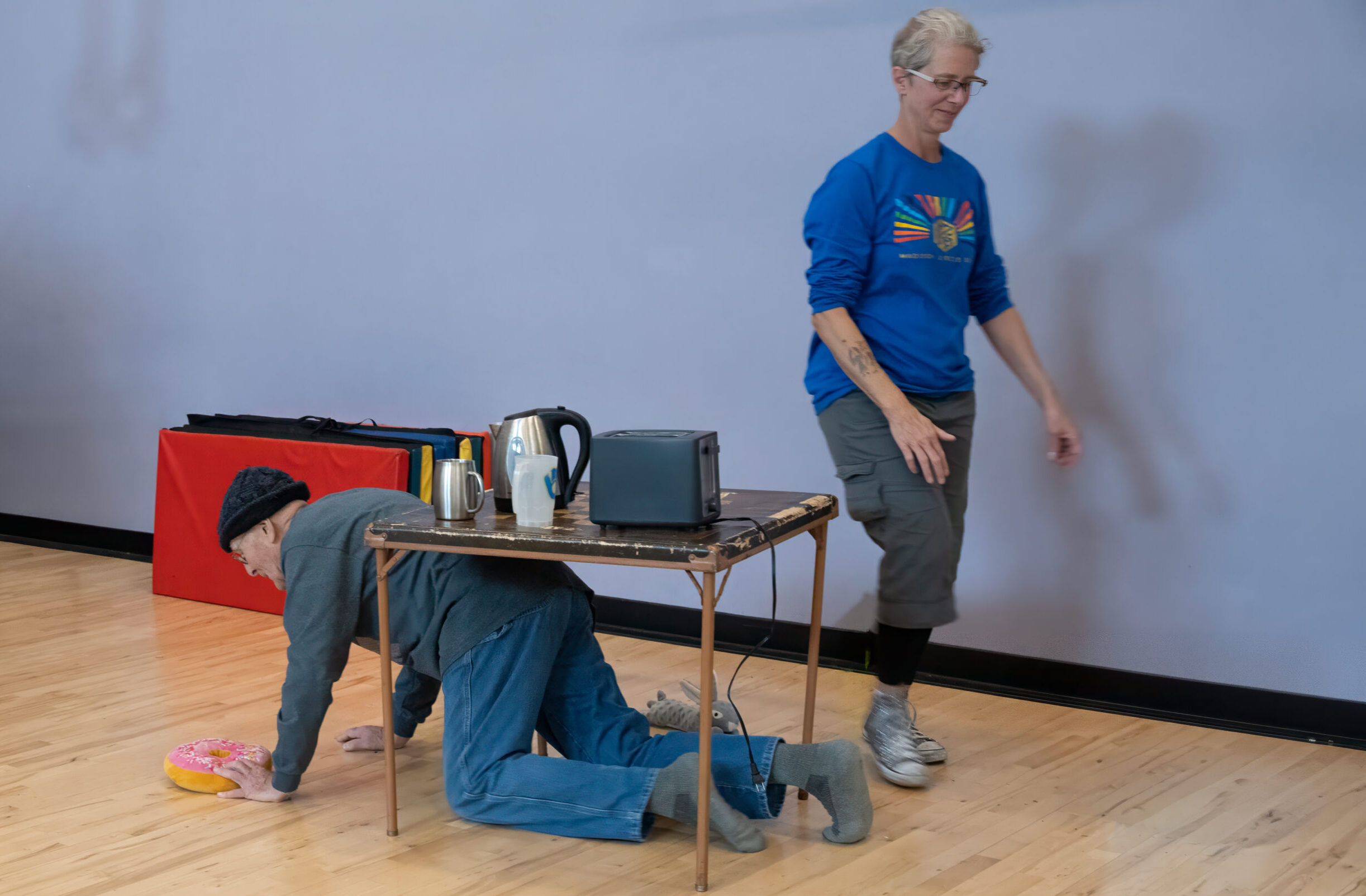 A person crawling under a table as another person stands by them