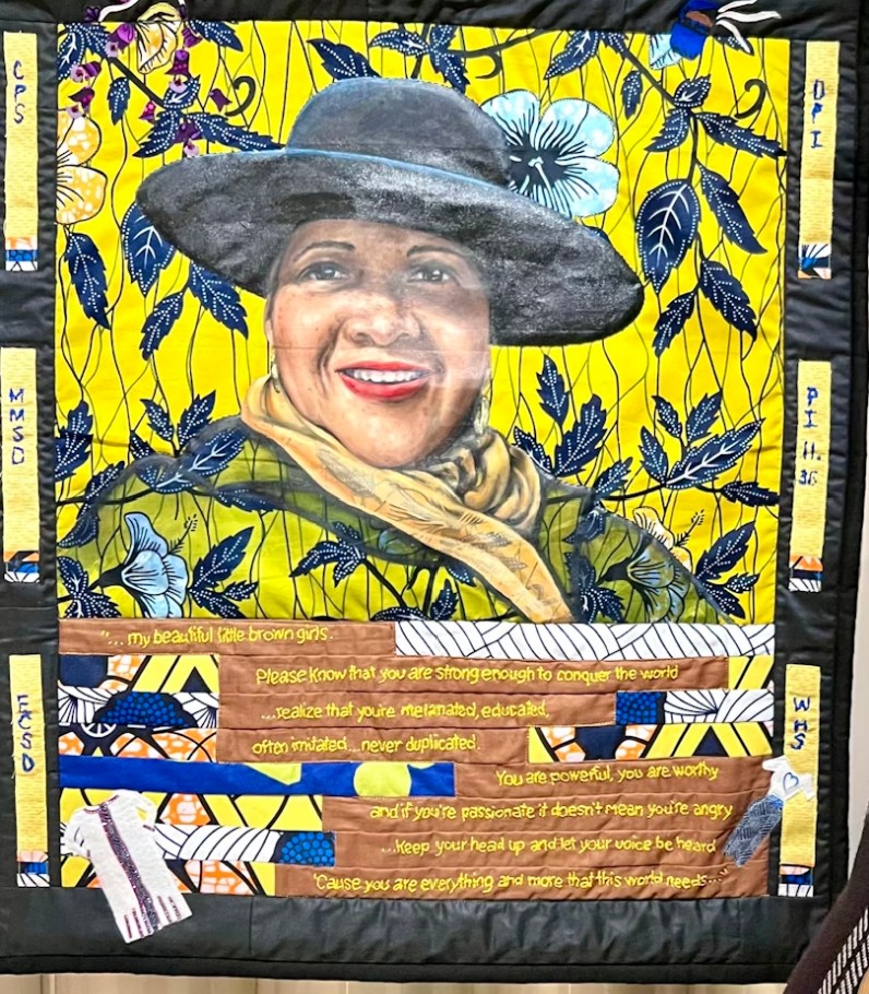 A yellow quilt with a woman, words, and flowers on it.