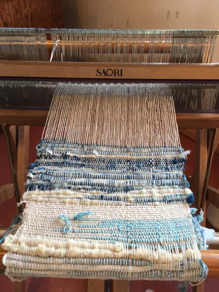 A loom strung with a partly woven garment of white and blue threads.