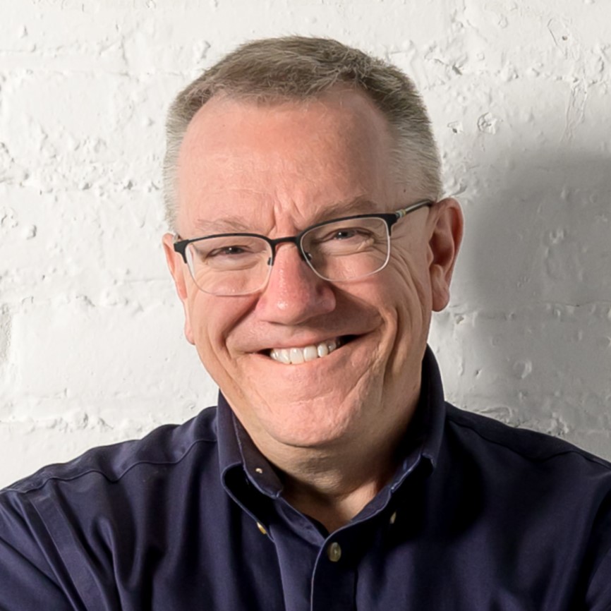 Headshot of photographer, Bre McGee from Uncommon Collaborative. He is smiling and has short hair and glasses wearing a dark shirt against a white wall.