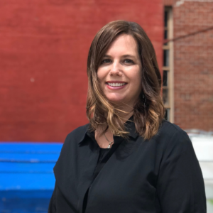 A woman with light skin tone and medium brown hair, wearing a black button-up shirt and smiling.