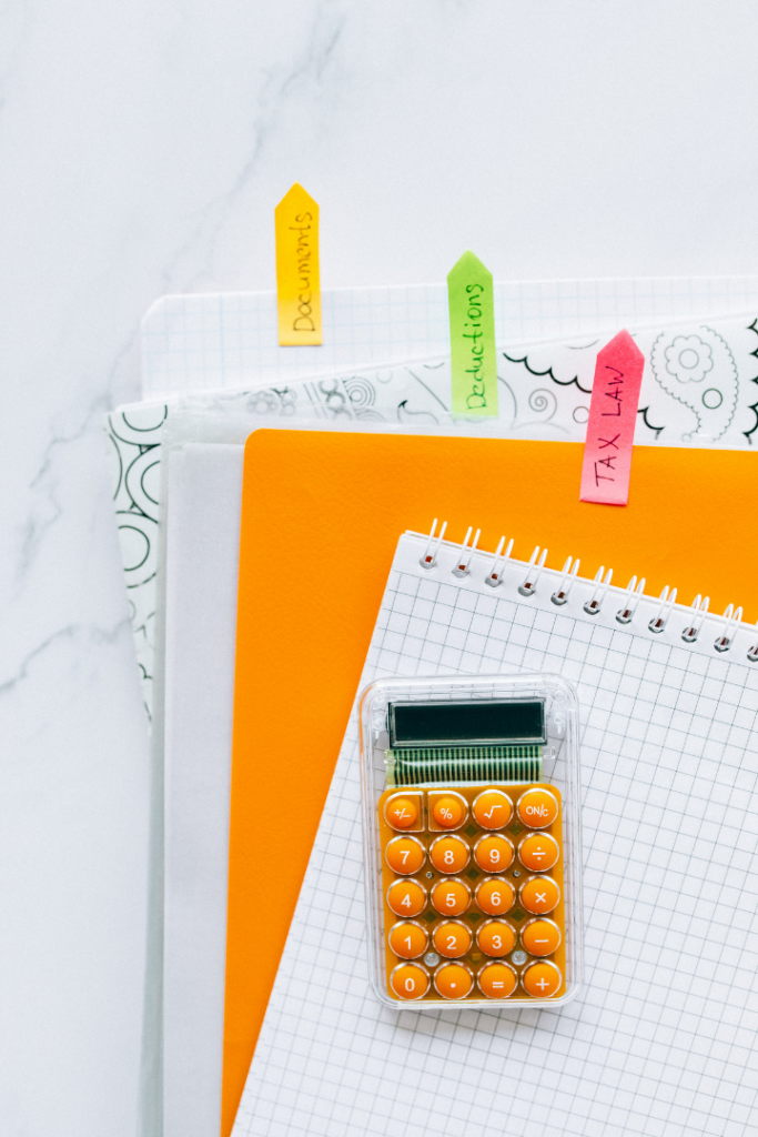 Calculator with orange buttons lying on top of spiral bound notebooks with color-coded tabs