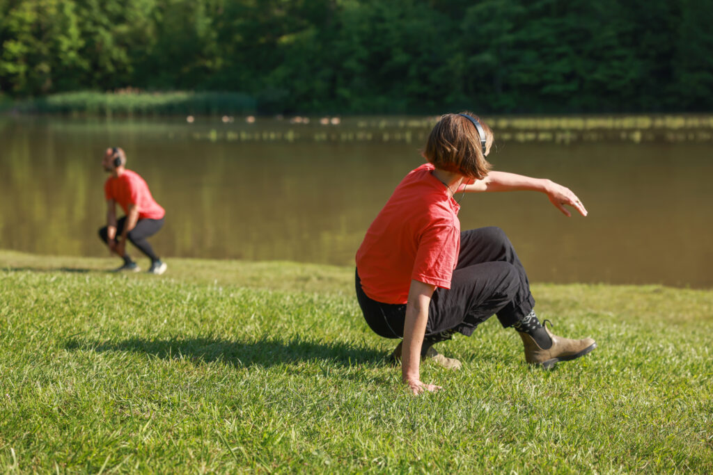 Two people moving their bodies outdoors on a grassy field.