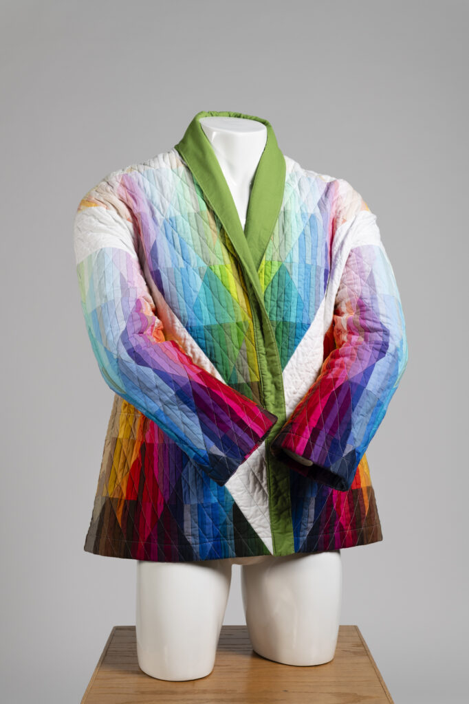 A multicolored quilted coat on a white mannequin with its arms crossed at the wrists.
