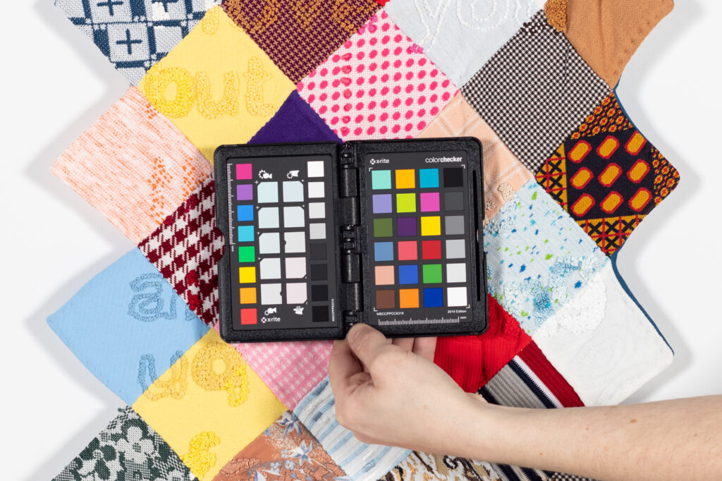 A hand holding a pallet of many color swatches over a multicolored section of a quilt.
