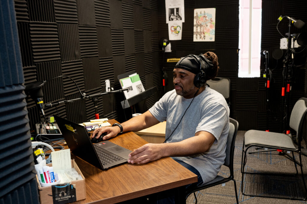 A person sitting at a table inside an audio recording booth.