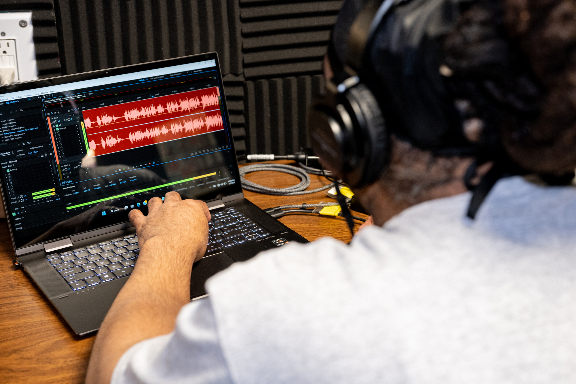 A person editing an audio clip on a laptop in front of them.