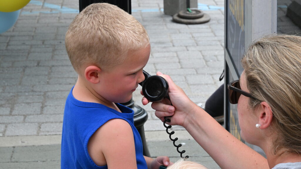 An adult holding a traditional phone to a child's ear.