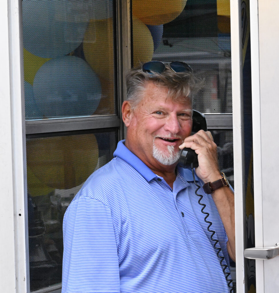 A person wearing a striped blue polo tshirt stands inside a phone booth talking into the handset