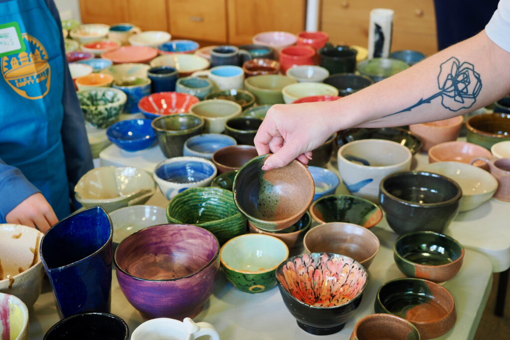 A light-skinned hand with a floral tattoo reaching for a bowl amid a table of other bowls.