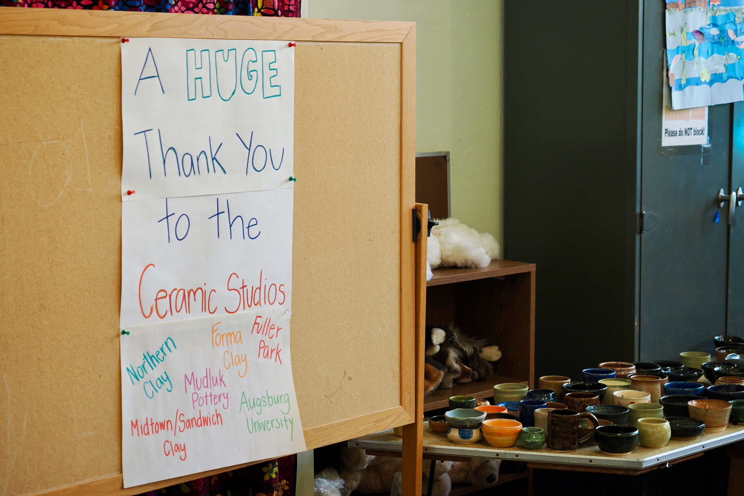 Bowls sitting on a table next to a sign reading: A HUGE thank you to the ceramic studios, followed by a list of several organizations written in different colors.