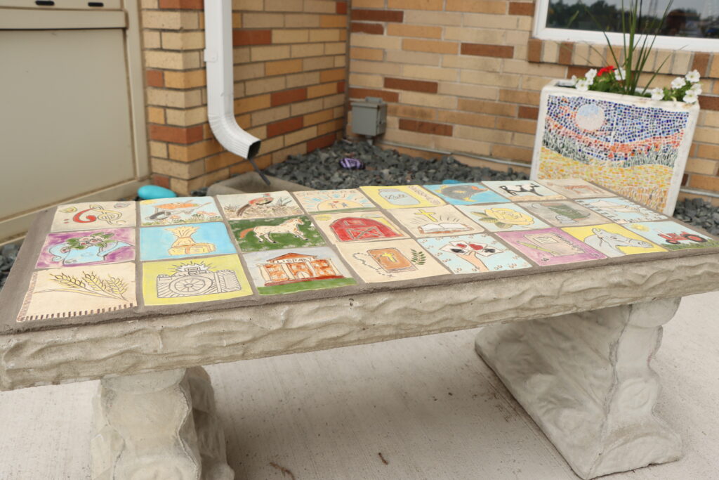 A concrete bench with a mosaic seat made of painted square tiles.