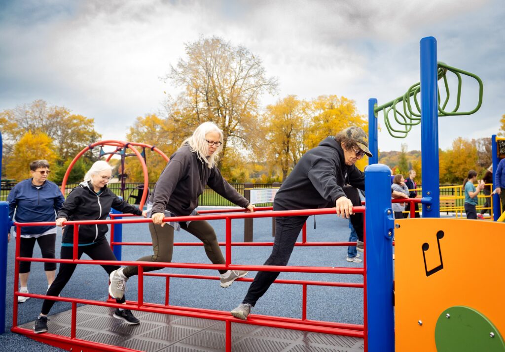 Three older people climbing on railings at a playground