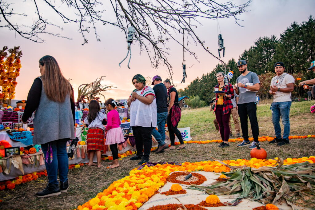 People standing outdoors around a large installation of an ofrenda that include marigold flowers and other sculptural items