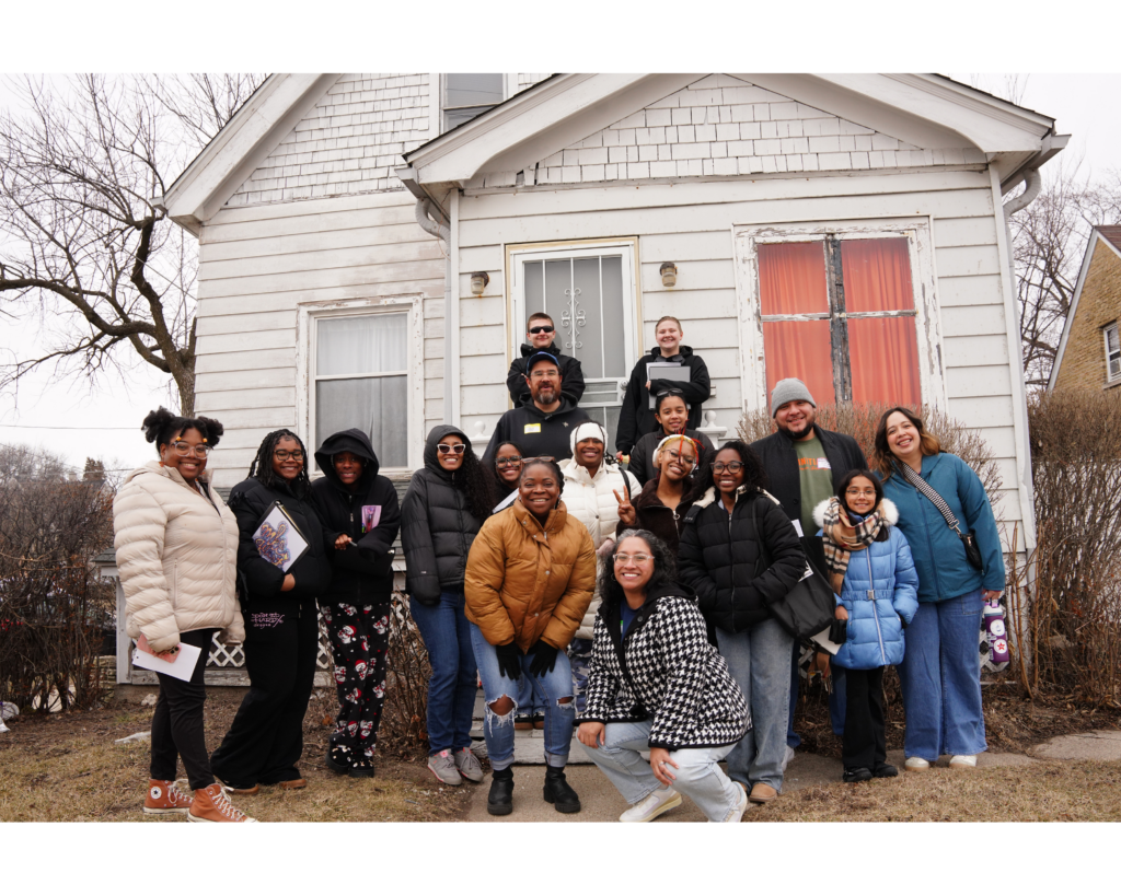 A group of people standing and posing in front of a white home.