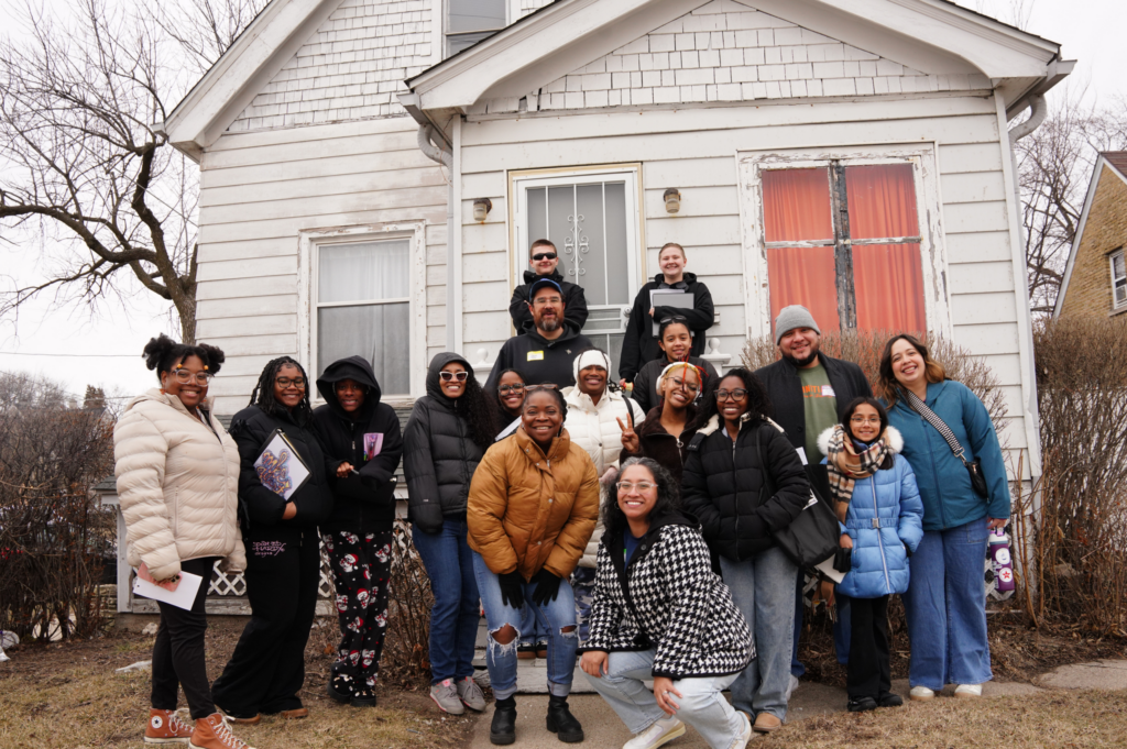 A group of people standing and posing in front of a white home.