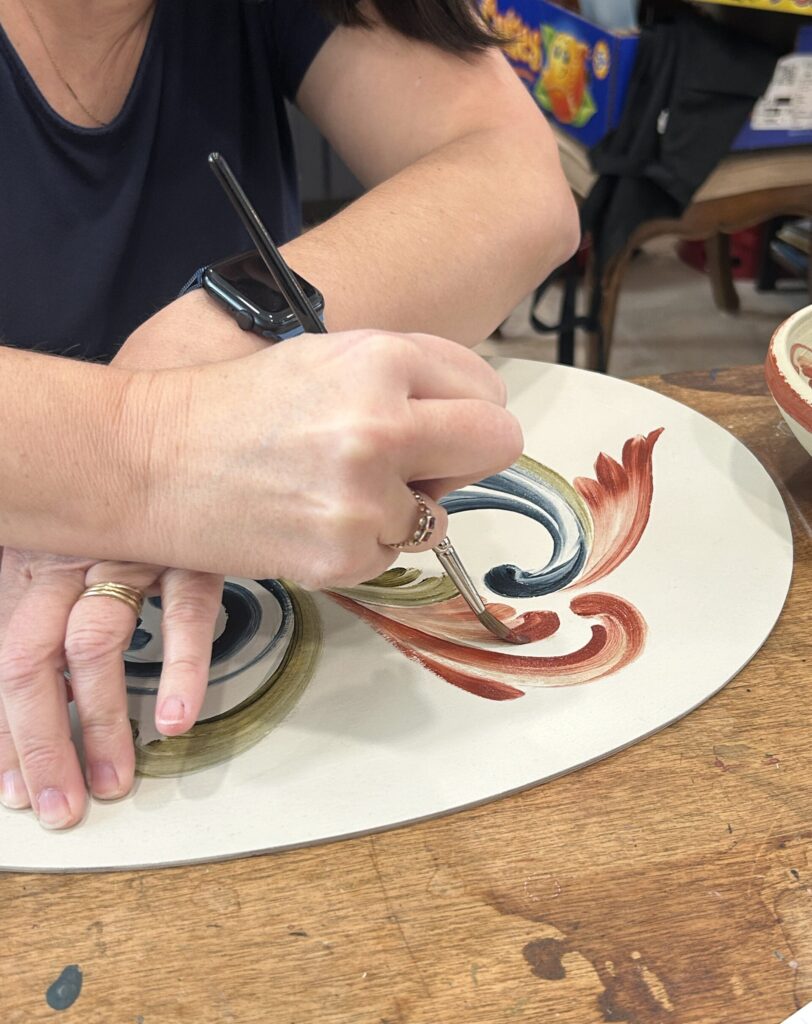 A person painting on a flat unfired pottery piece