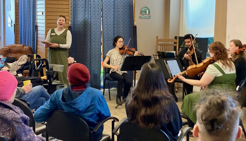 A group of classical musicians play in front of an audience in a room