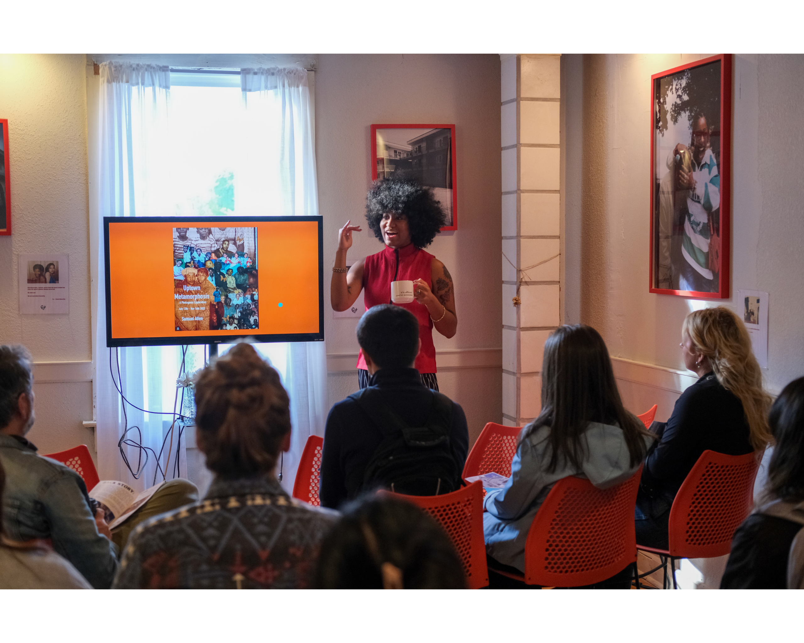 A woman with dark skin tone speaking and gesturing during a presentation to a crowd.
