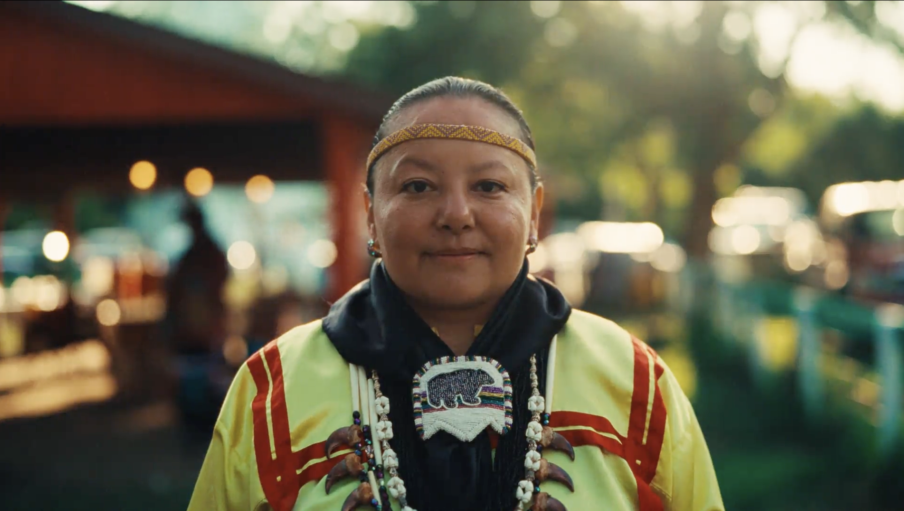 A person with medium skin tone looking at the camera and wearing traditional Meskwaki clothing.