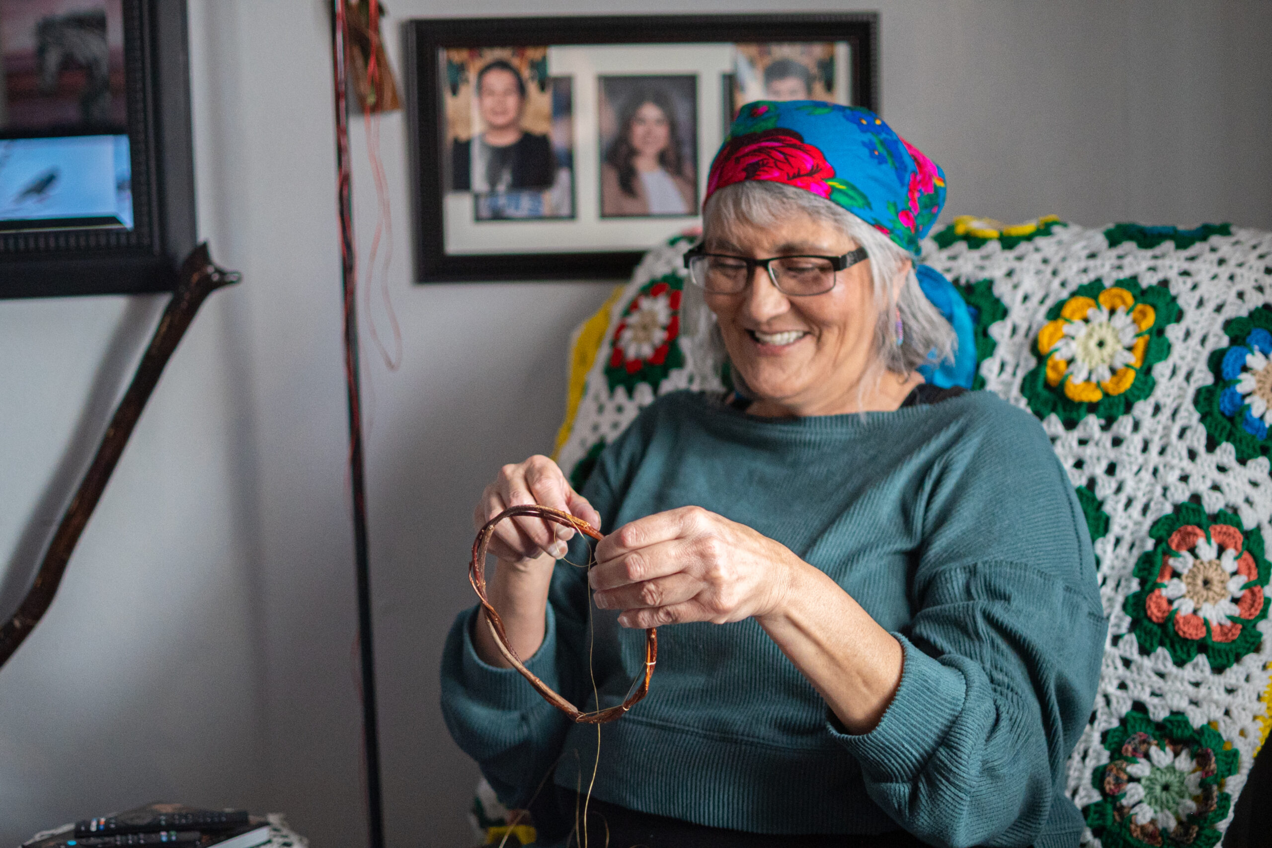 A person of light skin tone sitting and smiling on a couch as they start to make a dreamcatcher with willow and thread.