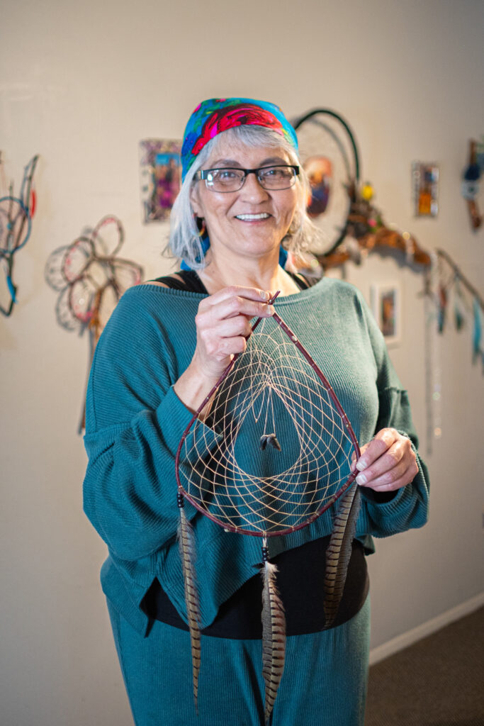 A person of light skin tone holding a dreamcatcher made with string, willow, feathers, and beads.