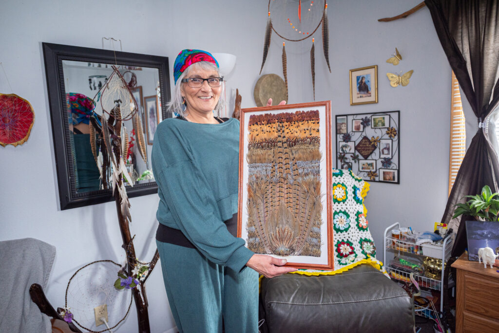 A person holding a framed artwork made with a variety of feathers