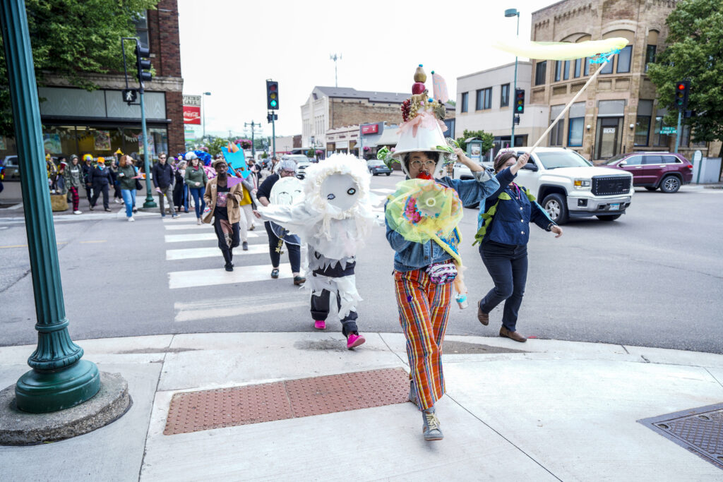 A group of people crossing a street. Some are wearing costumes.