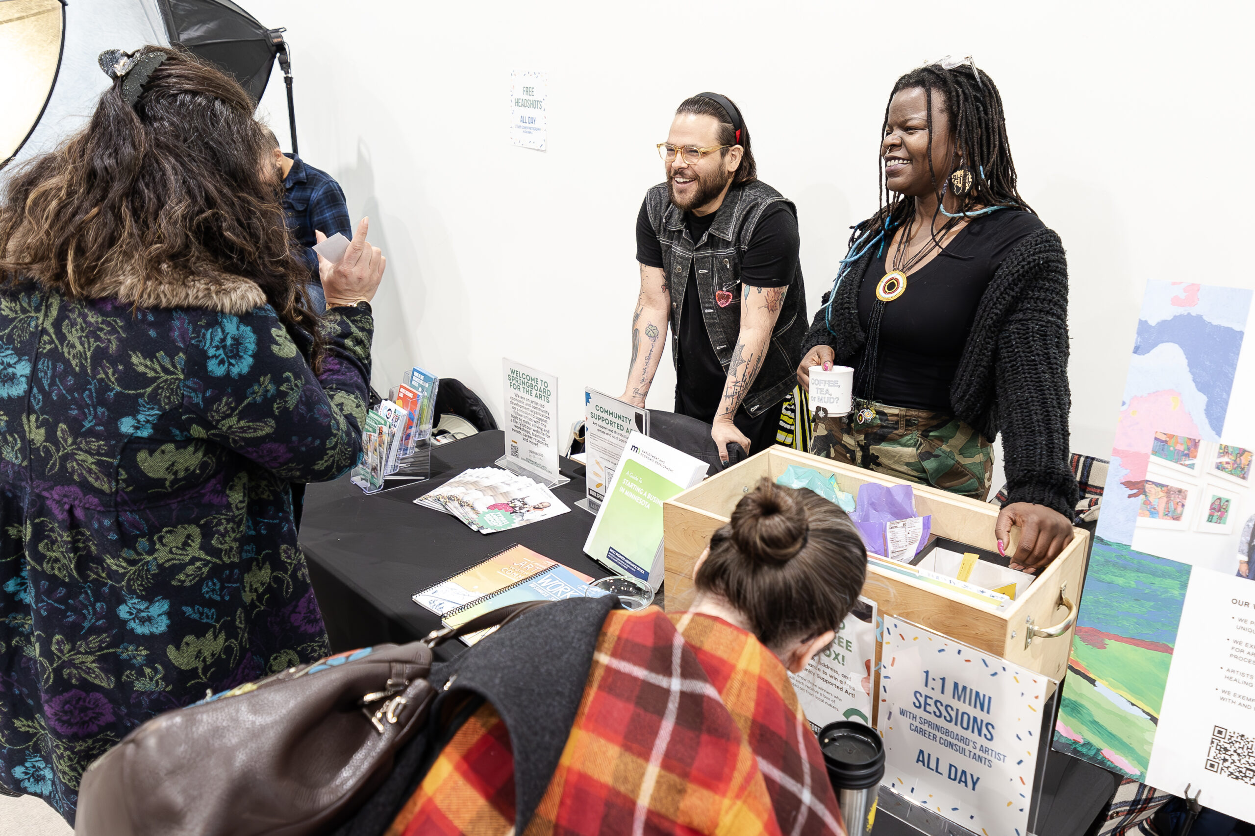 Two people smiling and talking to a person across from them. There is a table set up in front of them with different informational printed materials.