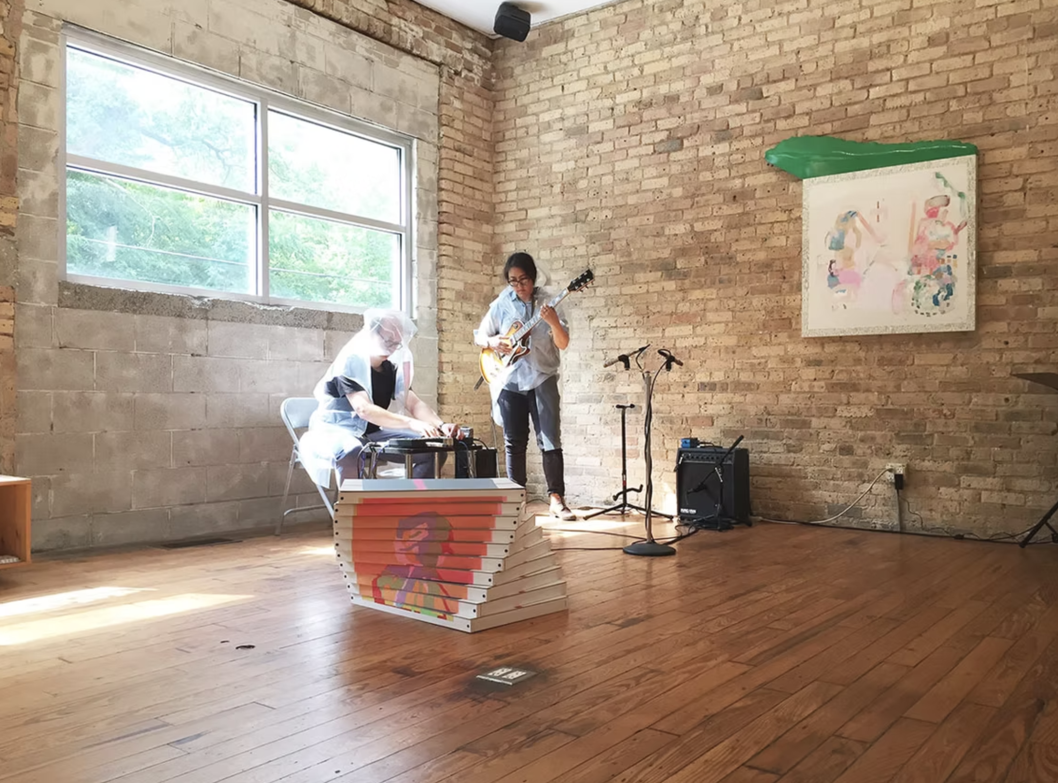 Two performers play guitar and an electronic mixer inside a brick building.