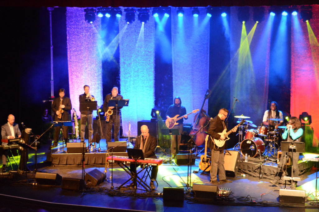 A stage with colorful lights and many jazz musicians performing.