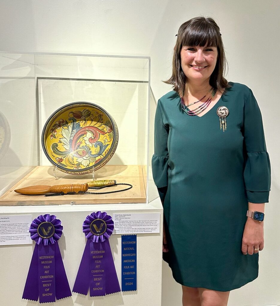 A person standing next to a hand painted bowl displayed on a pedestal with purple ribbons of recognition.