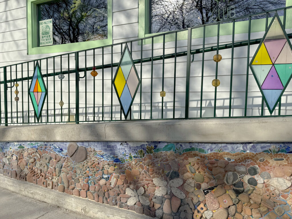 A side view of an artfully-made concrete accessibility ramp with a stone mosaic and glasswork on the railings