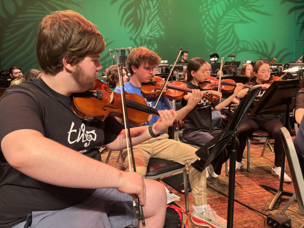 Students rehearsing on stage with violins.