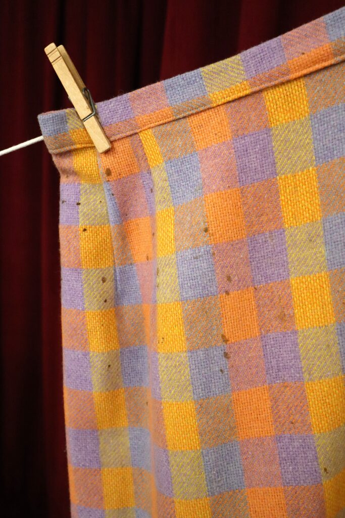 A plaid skirt with small spotted stains hanging on a clothesline.