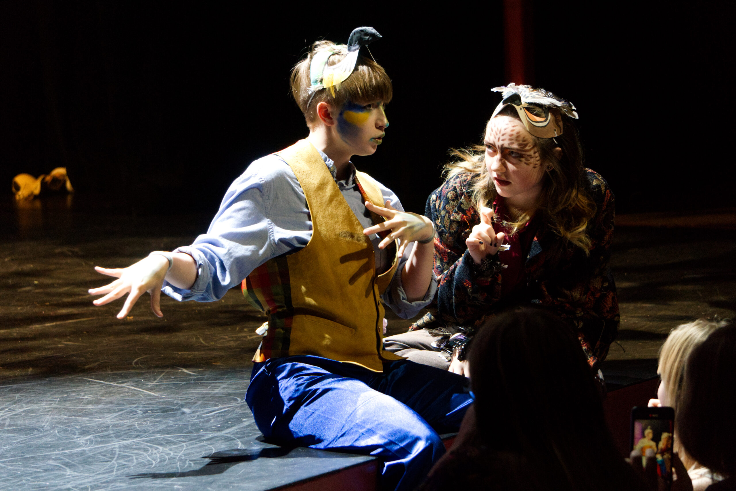 Two high school actors on a stage with masks and makeup.